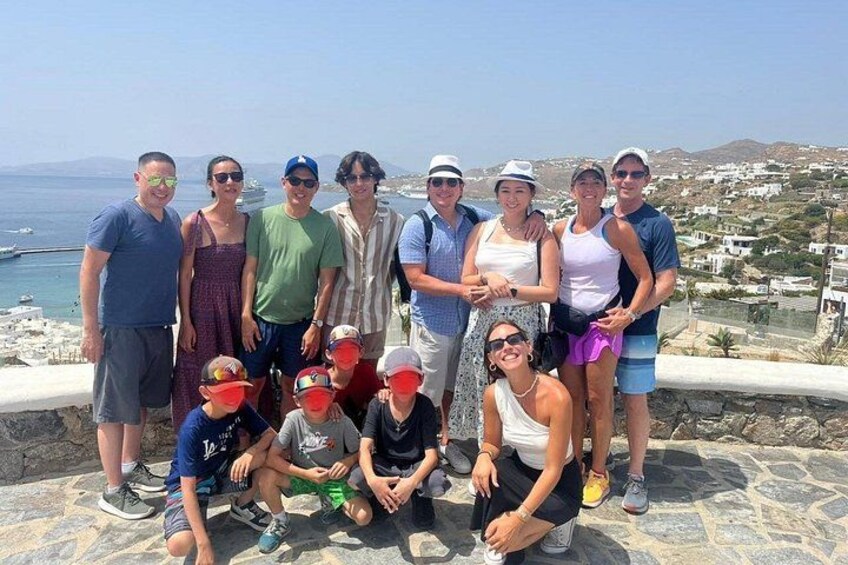 Un groupe de personnes posant sur une corniche en pierre, avec une ville côtière et un ciel dégagé en arrière-plan. 4