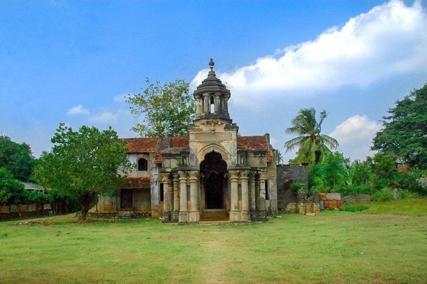 A historical building with a central archway and a bell tower, surrounded by greenery and palm trees. 3