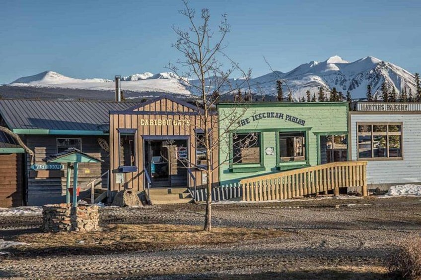 En rustik bygning med en grøn facade, der er skiltet 'The Ice Bean Parlor', en trækonstruktion med veranda og et bjerglandskab i baggrunden. 4