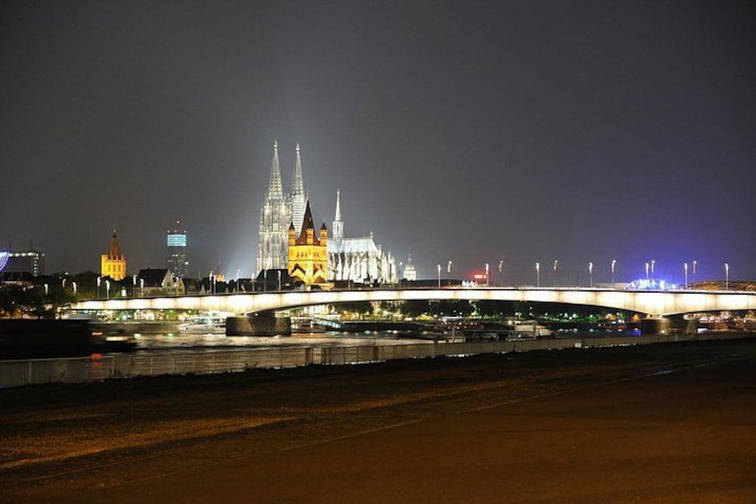 A nighttime view of a cathedral with two spires, a bridge, and city lights. 2