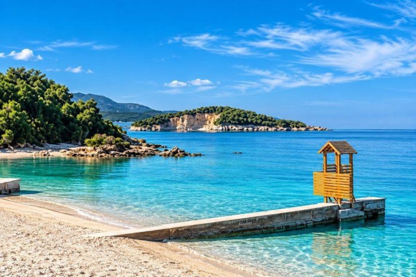 A beach with clear turquoise water, a wooden lifeguard tower, and a rocky island in the background. 5