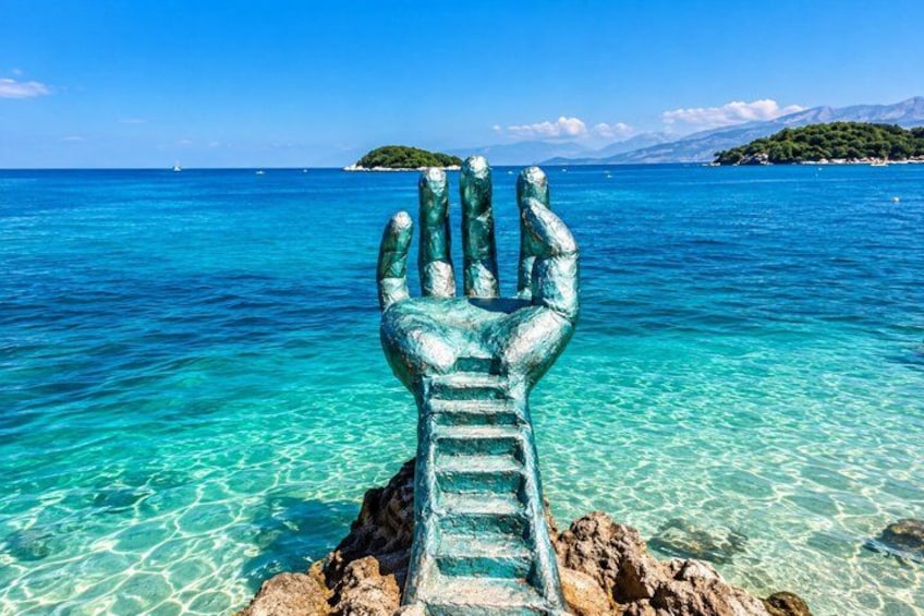 A hand sculpture in the water with clear blue sea and distant islands. 4