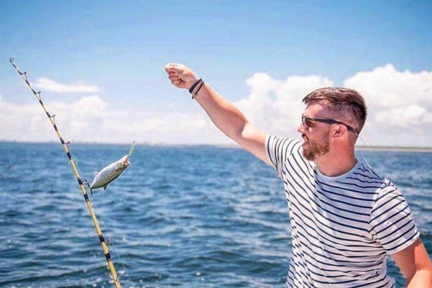 Una persona pescando con una caña y un pez enganchado, de pie en un bote en el océano. 2