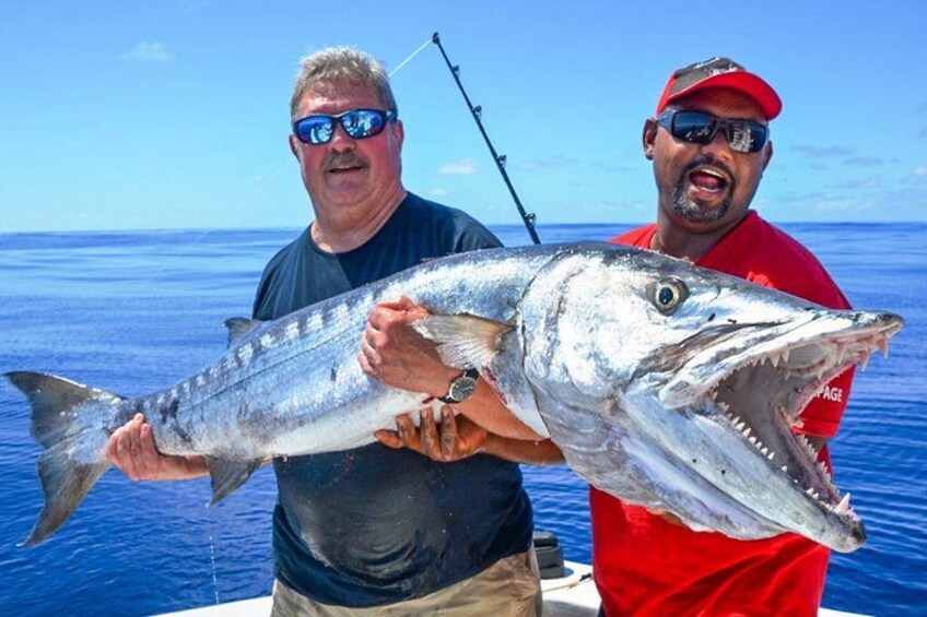 Deux personnes tenant un gros poisson sur un bateau, avec un ciel bleu clair et l’océan en arrière-plan. 1