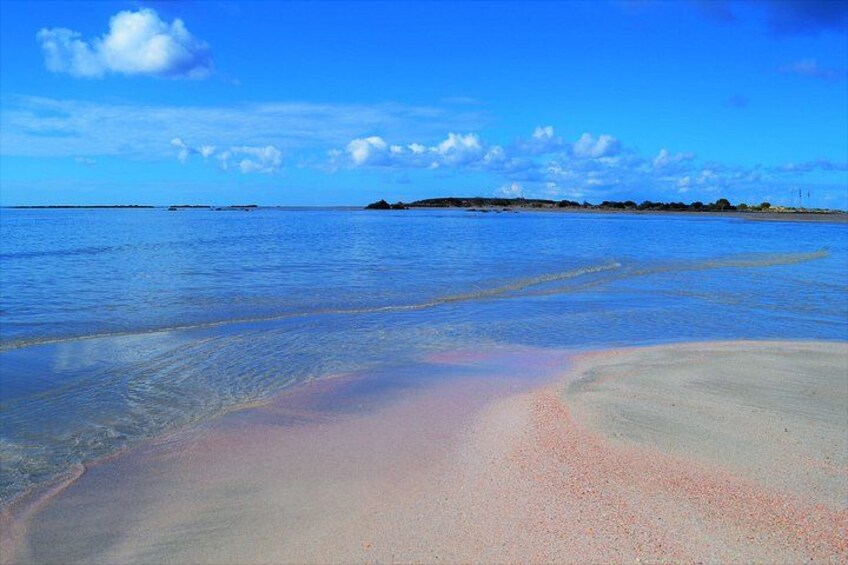 Una playa con agua azul cristalina, orilla arenosa y formaciones terrestres a lo lejos. 4