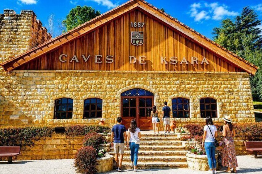 Un edificio in pietra con la segnaletica 'Caves de Ksara 1857', una facciata in legno e una scala che conduce all'ingresso. 3