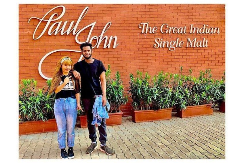 A brick wall with the text 'Paul John The Great Indian Single Malt' and two people standing in front of it. 1