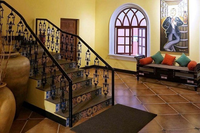 A staircase with ornate metal railings, a large vase, a bench with colorful cushions, and a window with a view. 5