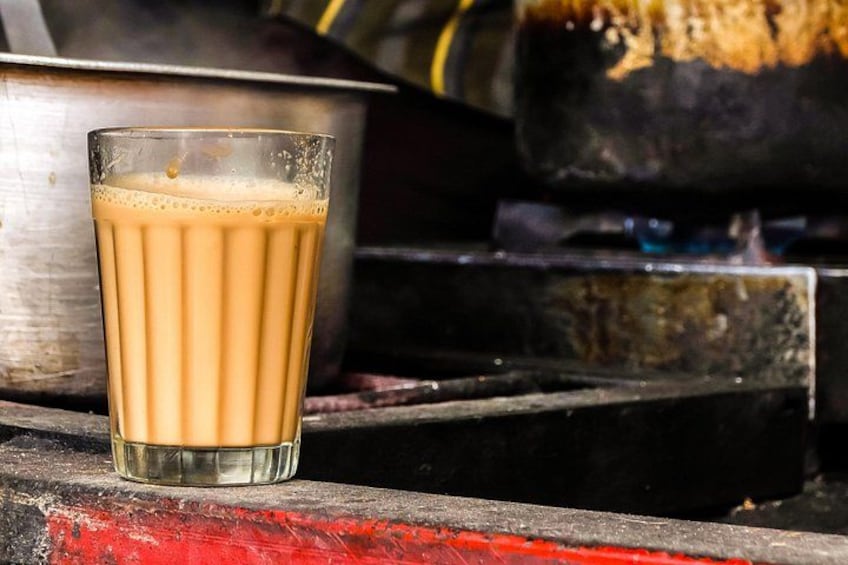 Une tasse de thé chai posée sur une surface métallique, avec une théière en arrière-plan. 2