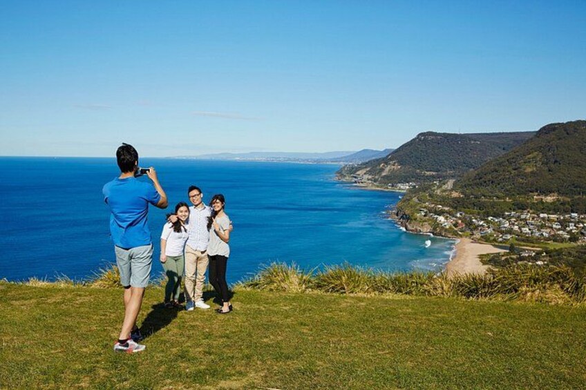 Un grupo de personas en una colina cubierta de hierba, con vista a un pueblo costero y una playa, y colinas lejanas. 5