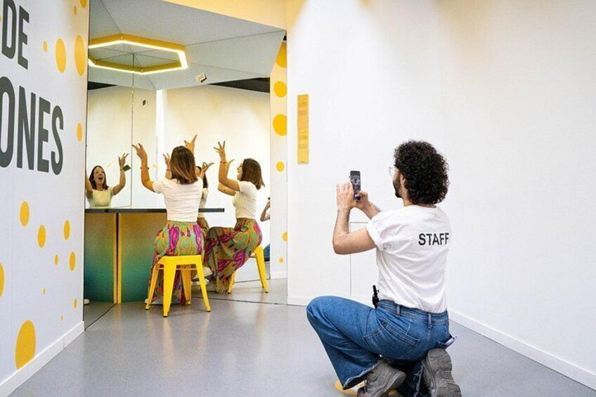 Un estudio de baile con un espejo grande, un taburete amarillo y una persona tomando una fotografía. 3