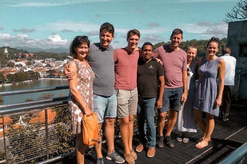 Un groupe de personnes se tient sur un balcon, d’où l’on peut admirer une vue sur la ville, avec un plan d’eau et des montagnes en arrière-plan. 5