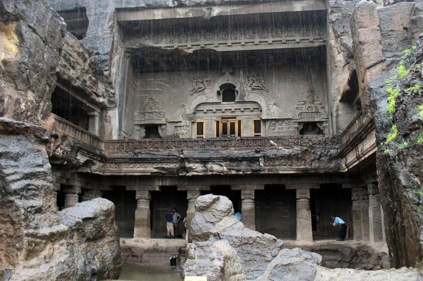A historical rock-cut temple with intricate carvings and a rainwater cascade. 1