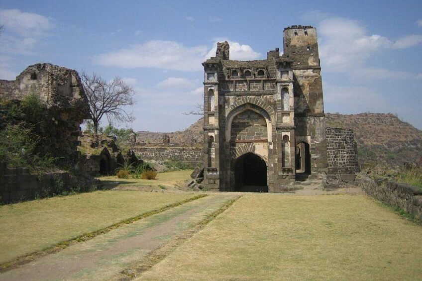 An ancient stone archway with a tower, surrounded by grassy terrain and ruins. 5