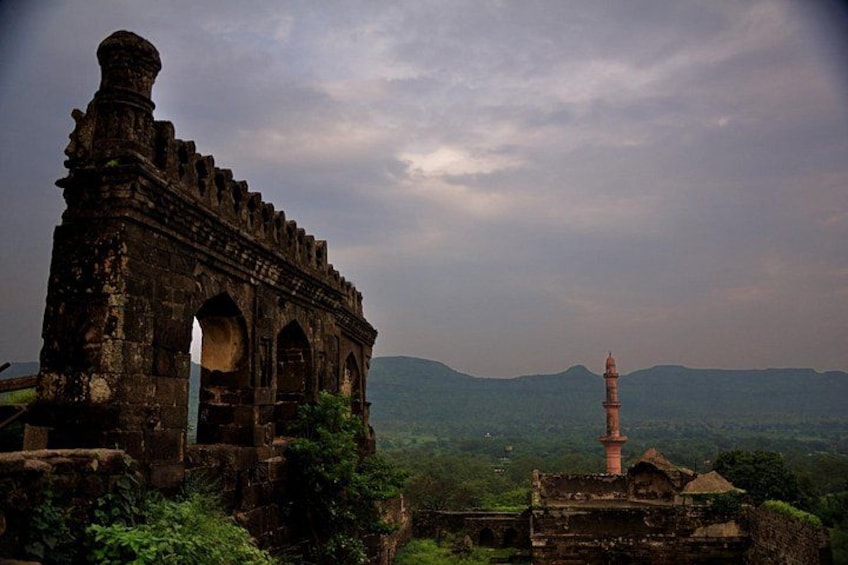 An ancient stone structure with arches and a tower in a lush, hilly landscape. 2