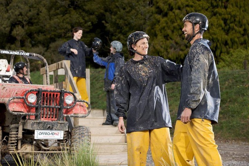 People in muddy clothing and helmets, a red off-road vehicle, and a wooden ramp. 2