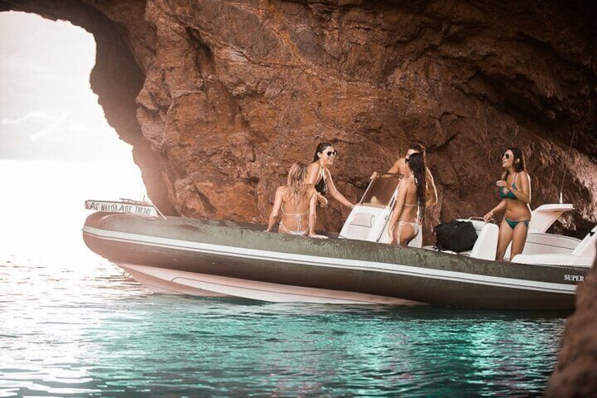 A boat with three people in bikinis near a rocky shoreline. 3
