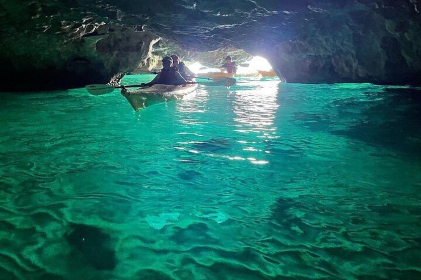 A cave with clear turquoise water and a person kayaking inside. 2
