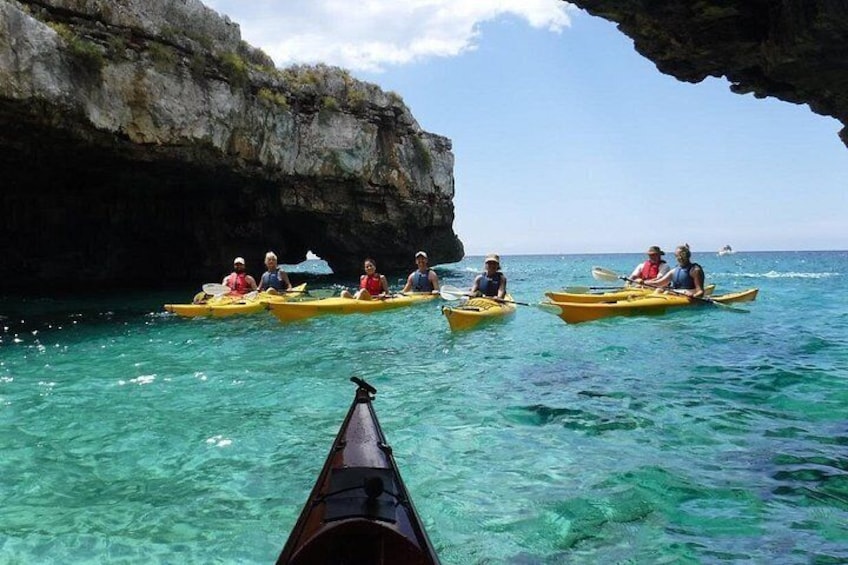 A group of people kayaking in clear turquoise water, with a rocky cliff in the background. 3