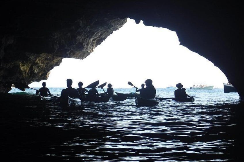People kayaking in a cave opening with water and boats in the background. 4