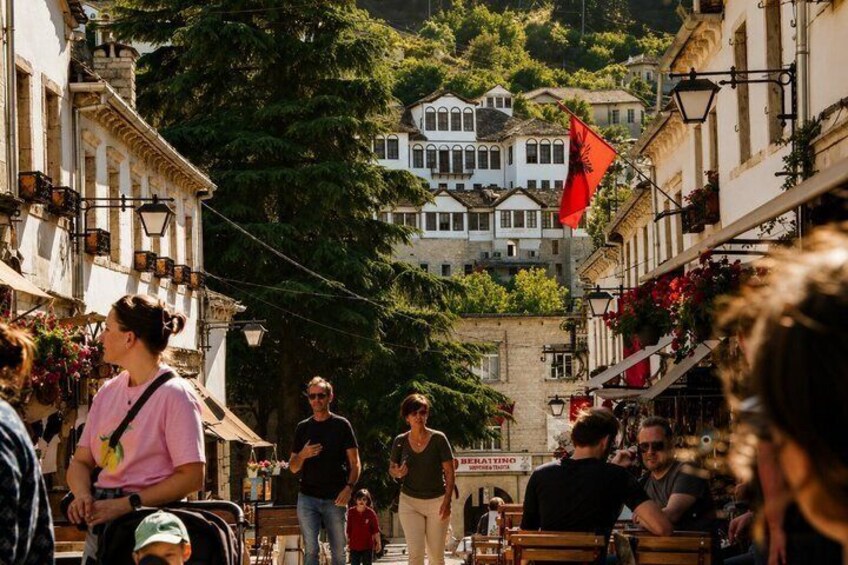 A bustling street with people walking, shops, and buildings with balconies. 1