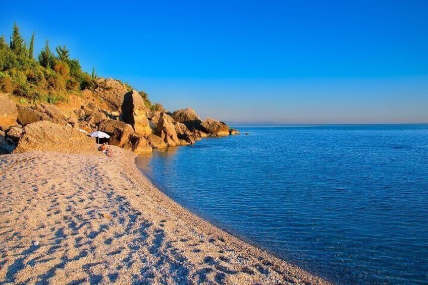 A sandy beach with footprints, a person with an umbrella, and rocky outcrops. 1