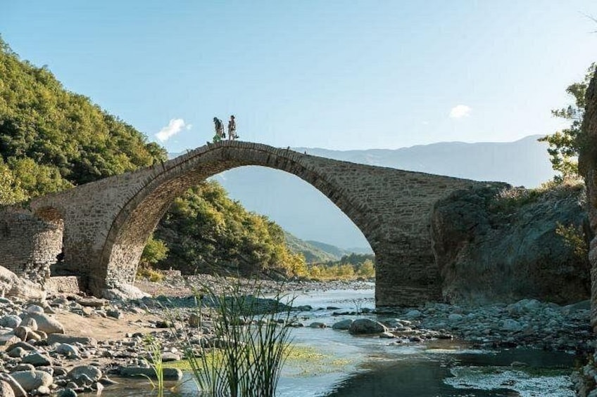 An ancient stone bridge over a river, surrounded by rocky terrain and greenery. 2