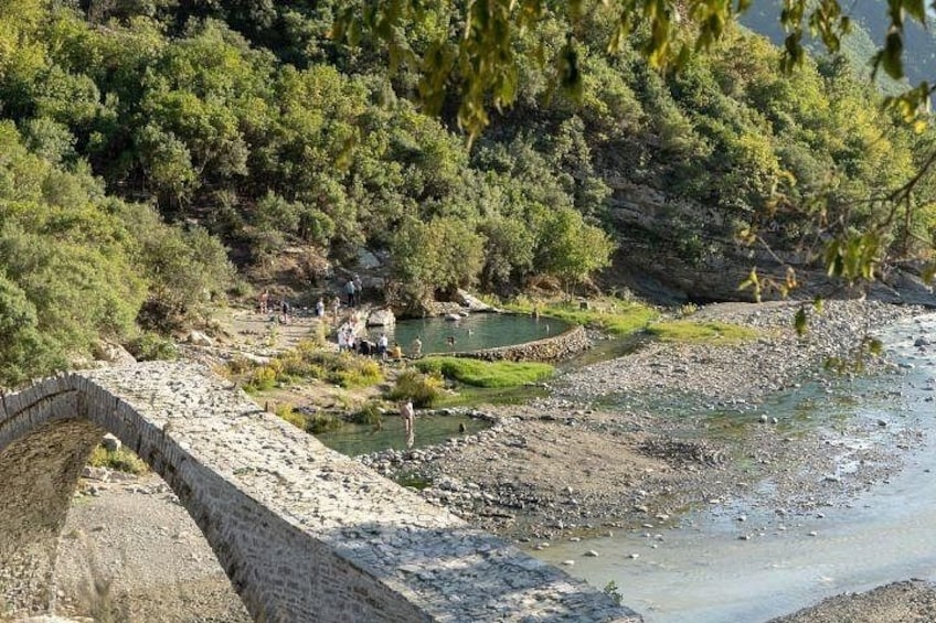 A riverbank with a stone bridge, greenery, and people near the water. 3