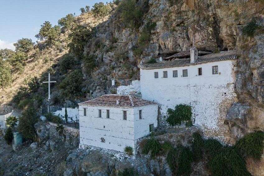 Een wit gebouw met een kruis, omgeven door rotsachtig terrein en begroeiing. 1