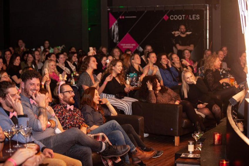 Een binnenevenement met zittende deelnemers, een podium en een banner met tekst. 3