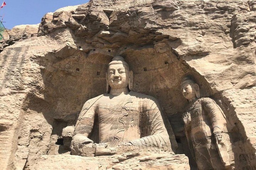 A large Buddha statue carved into a rock face, with intricate patterns and smaller figures around it. 1