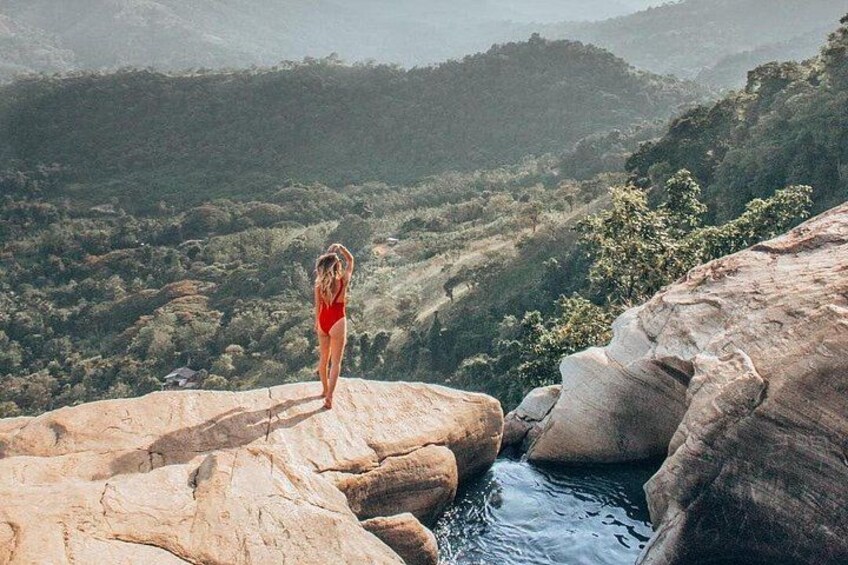 A person in a red swimsuit standing on a rock overlooking a valley with a river. 1