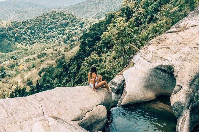 A person sitting on a rock by a water body surrounded by a forested landscape. 3