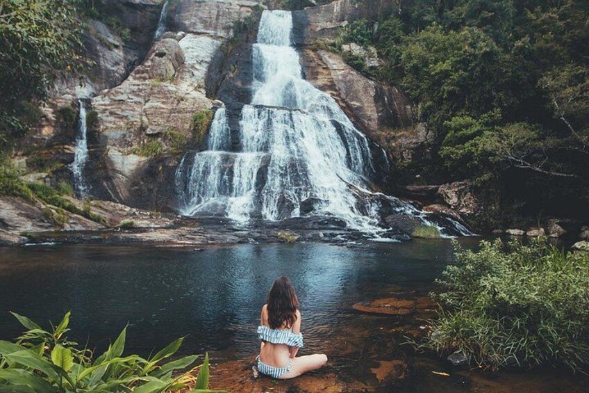A waterfall, a person sitting by the water, and surrounding greenery. 2
