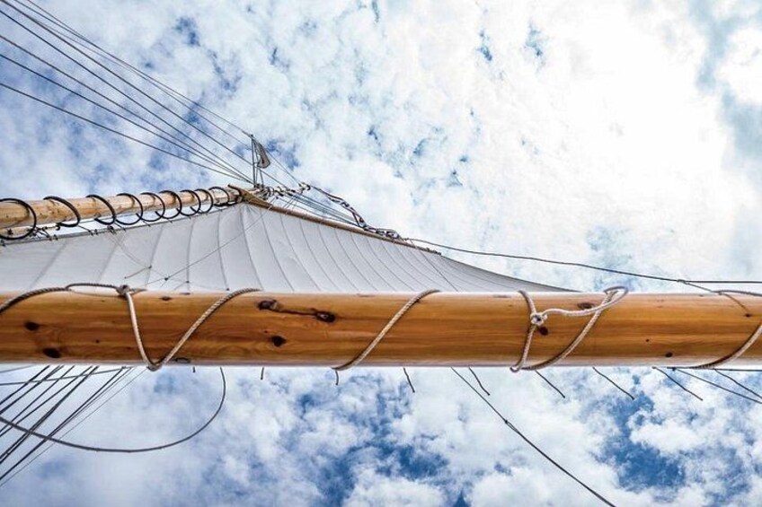 Een detailopname van een scheepsmast met lijnen en zeilen voor een bewolkte lucht. 5