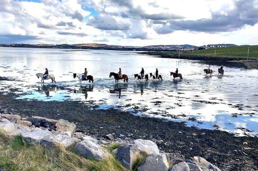 A group of people riding horses on a lake surrounded by rocks and grass. 4