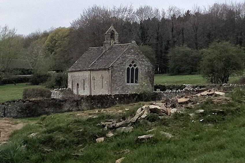 A stone church with a pointed roof and arched windows, surrounded by a grassy field and trees. 4