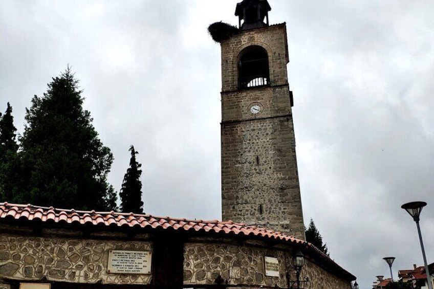 A stone tower with a clock, surrounded by trees and a tiled roof. 2