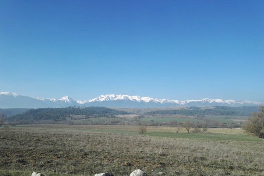 A mountain range with snow-capped peaks, a flat field in the foreground, and a clear blue sky. 5