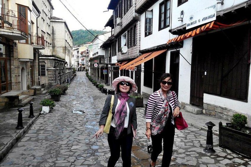 A cobblestone street lined with buildings, a person holding a camera, and another person walking. 4