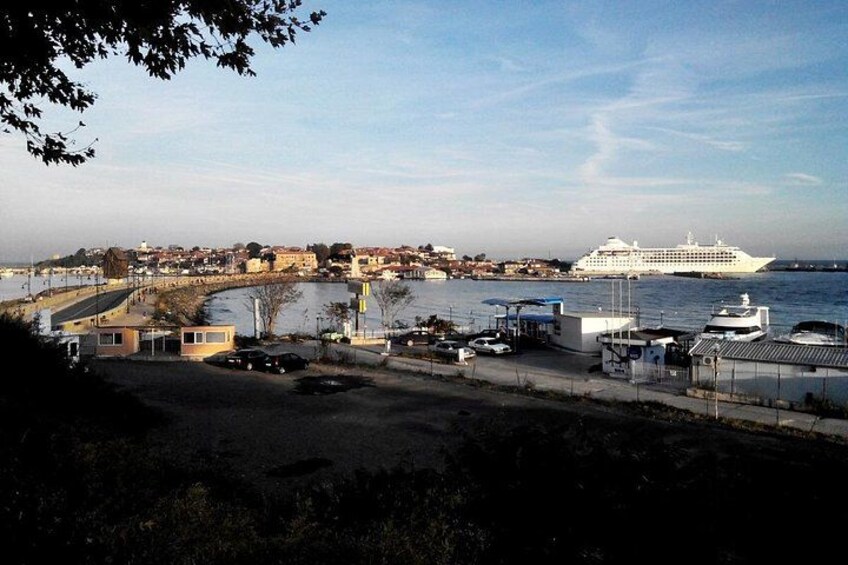 A coastal town with a large cruise ship docked, a marina with boats, and a bridge in the background. 2