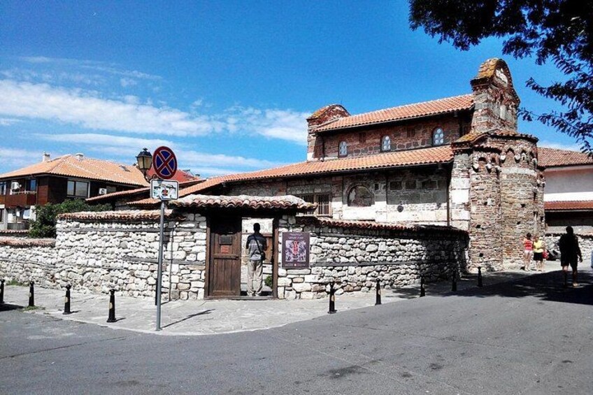 A stone building with a tiled roof, a stone wall, and a signpost with a no parking symbol. 4