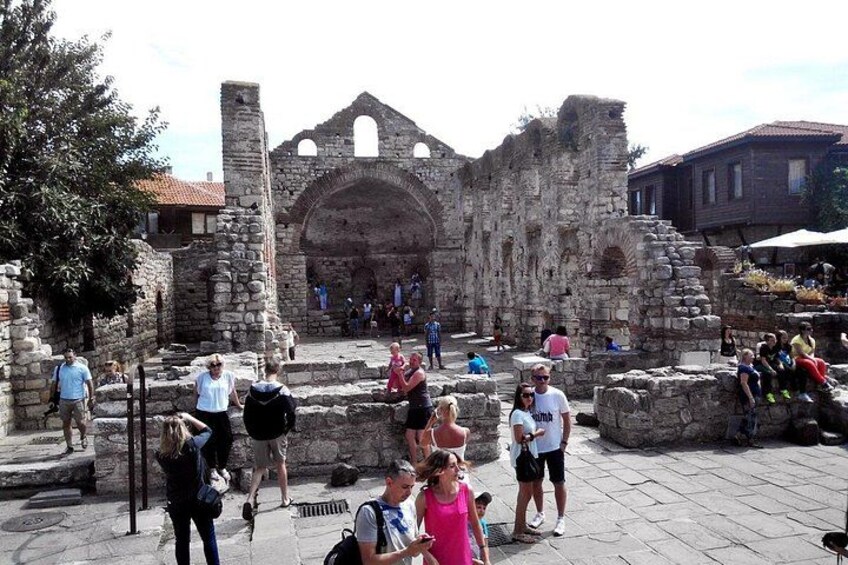 An ancient stone structure with arches and ruins, surrounded by people and a market. 5