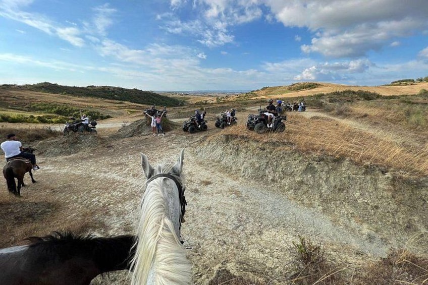 A horse and riders on a dirt trail with a hilly landscape in the background. 5
