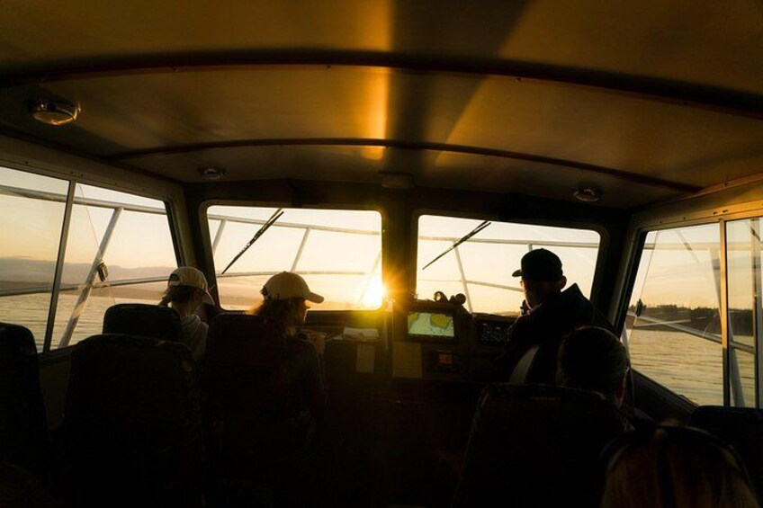 A boat interior with people, a steering wheel, and a view of the sunset. 2