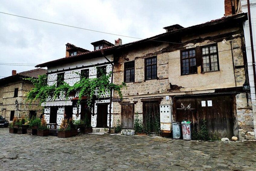 A cobblestone street with old stone buildings, some with ivy, and a few utility boxes. 5