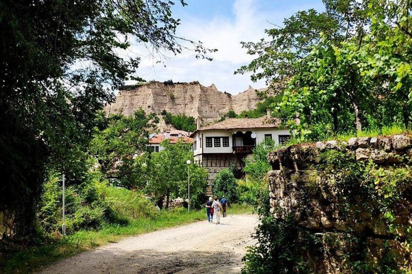 A dirt path leading to a historic building with a stone wall and trees. 4