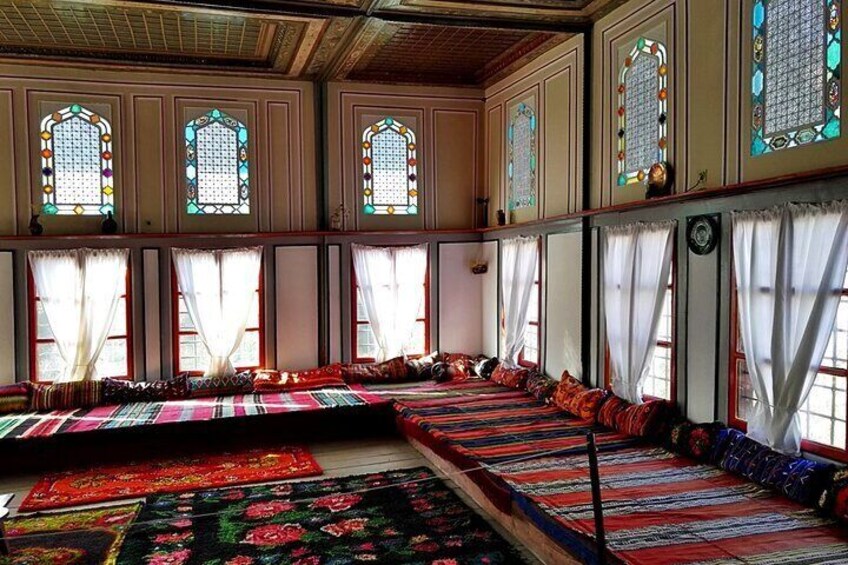 A prayer hall with rows of prayer rugs and benches, large stained glass windows, and white curtains. 1