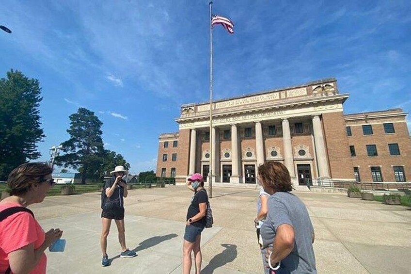 Un grupo de personas frente a un gran edificio con columnas y una bandera estadounidense. 1