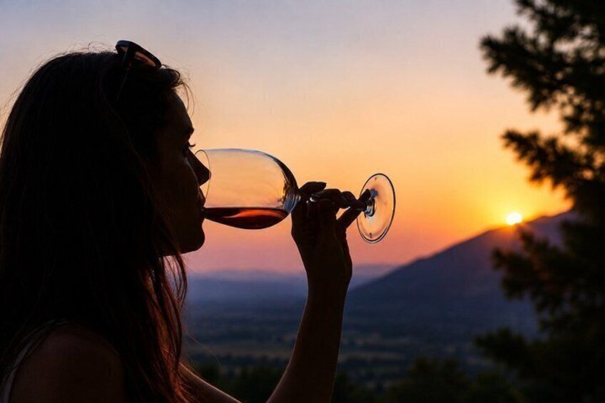 Een persoon met een wijnglas, met een zonsondergang en bergen op de achtergrond. 2